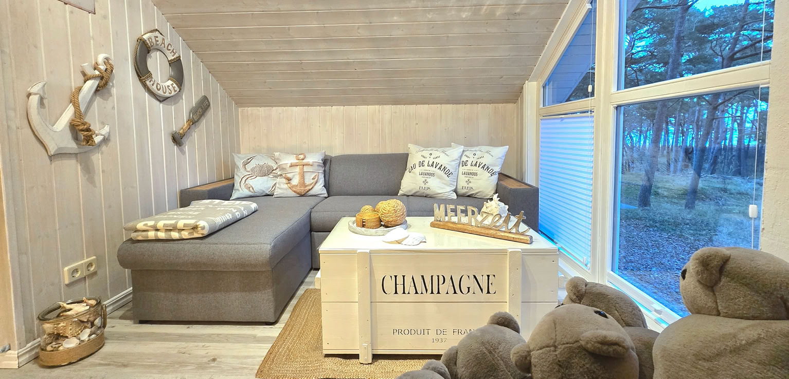 Gemütlicher Raum mit Dachschräge, rosa Sofa, rundem Sessel mit Plüschtieren, großen Fenstern und der Aufschrift "Pink and More" an der Wand.