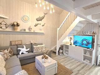 Wohnbereich im maritimen Stil mit gemütlicher großer Sofaecke, Fußbodenheizung, Fernseher und heller Holzgestaltung. Offene Galerie mit Treppe und liebevollen Dekorationselementen schafft eine freundliche und einladende Atmosphäre. 