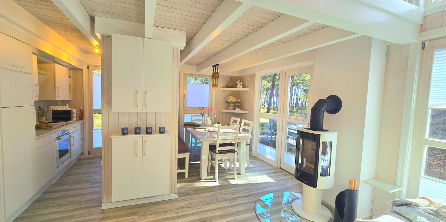 Heller Wohn- und Essbereich mit Kamin, großen Fensterfronten und Blick auf die Ostsee. Vom Sofa aus lässt sich der Meerblick genießen, während die offene Gestaltung für eine freundliche und entspannte Urlaubsatmosphäre sorgt.