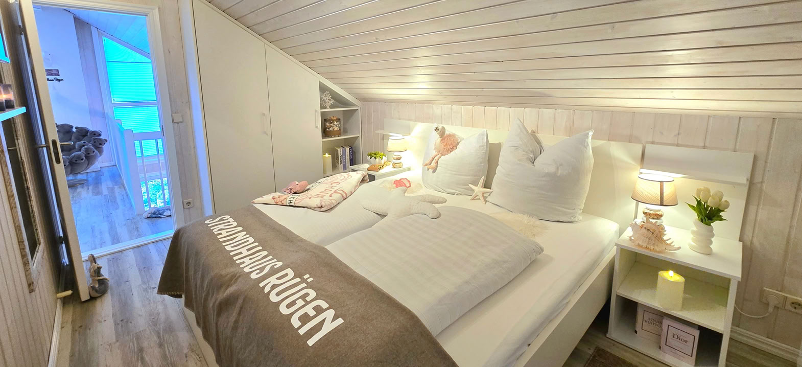 Gemütliches 2. Schlafzimmer im OG auf der Galerie mit Doppelbett, Fernseher mit Streaming-Diensten und praktischen Einbauschränken. Der direkte Zugang zum Balkon sowie die helle Holzgestaltung schaffen eine entspannte Atmosphäre für erholsame Urlaubstage nahe der Ostsee.