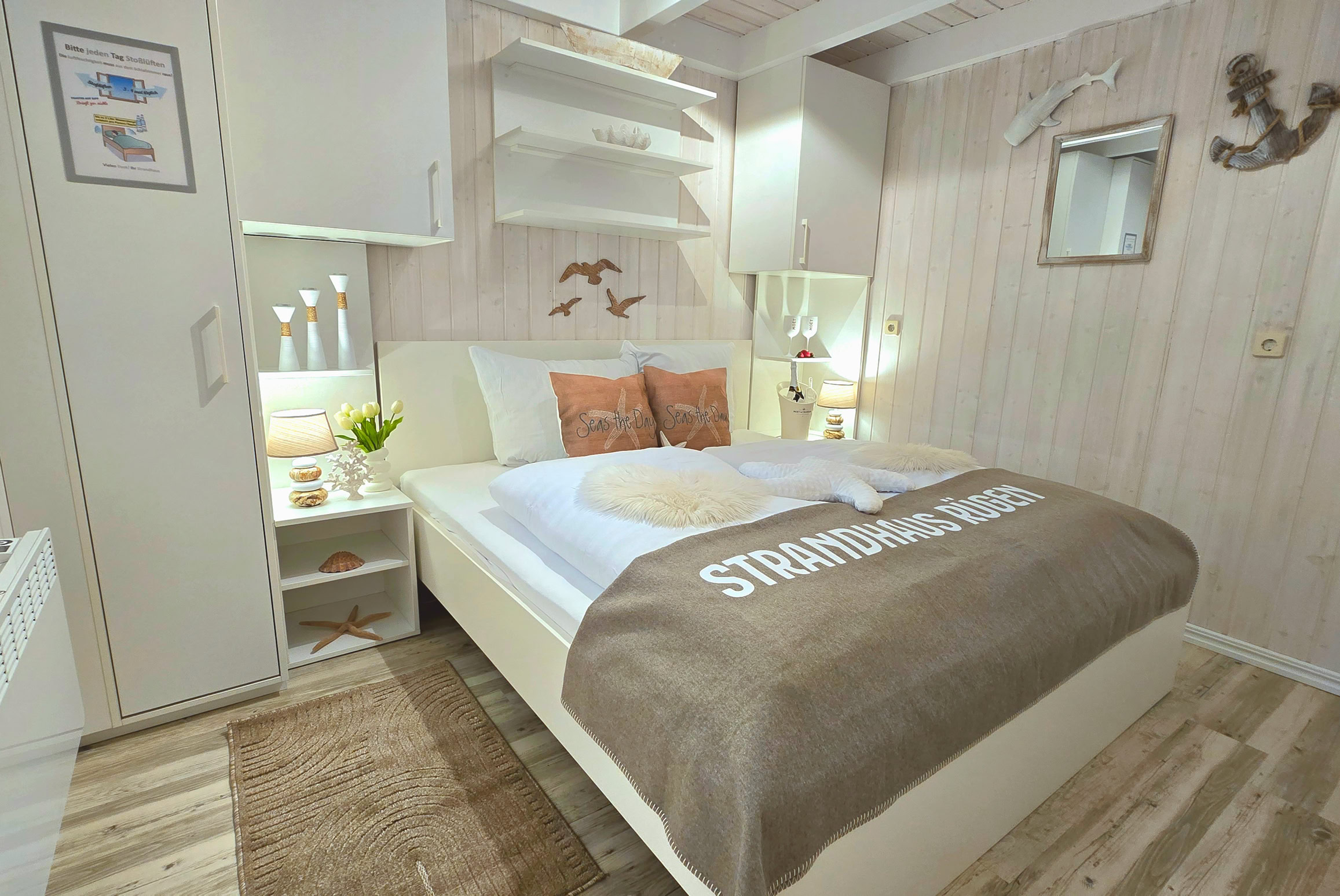 Schlafzimmer im Erdgeschoss mit Doppelbett, Fenster, großzügigen Kleiderschränken und maritimer Einrichtung. Gegenüber befindet sich das Badezimmer. Ein Fernseher mit Streaming-Diensten sorgt für zusätzlichen Komfort und entspannte Abende.